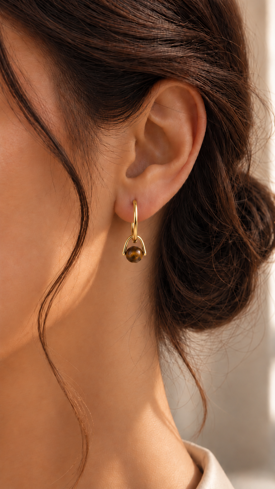 Boucle d’oreille Éclat dorée portée, avec une pierre brune aux reflets dorés